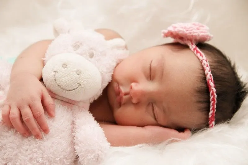Nyfødt jente som har på seg et strikket pannebånd og holder en teddy mens hun sover.