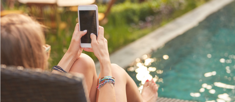 Девушка пользуется мобильным телефоном, лежа возле бассейна 