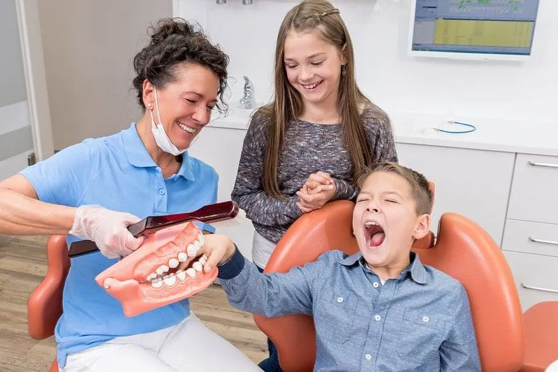 Barn som tuller med tannlegen og later som de fanger guttens fingre i gigantiske falske tenner.