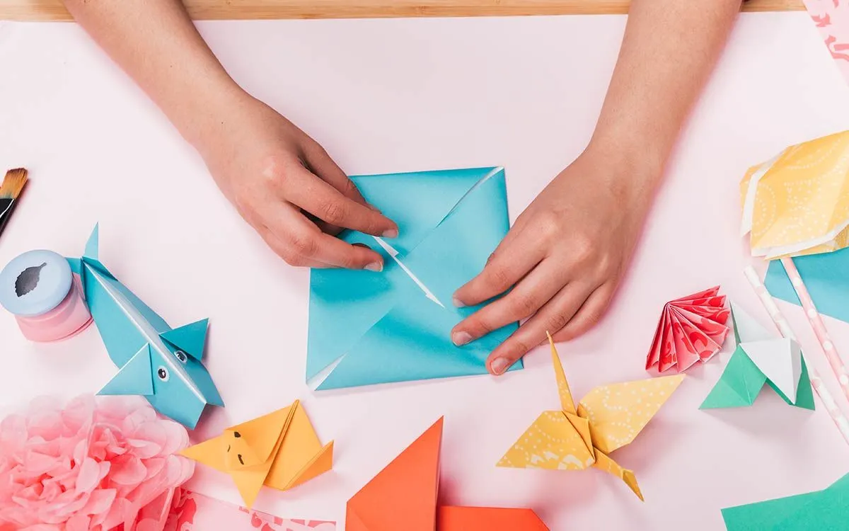 Egy gyermek keze egy origami papírdarabot hajtogatva origami pókot készít.