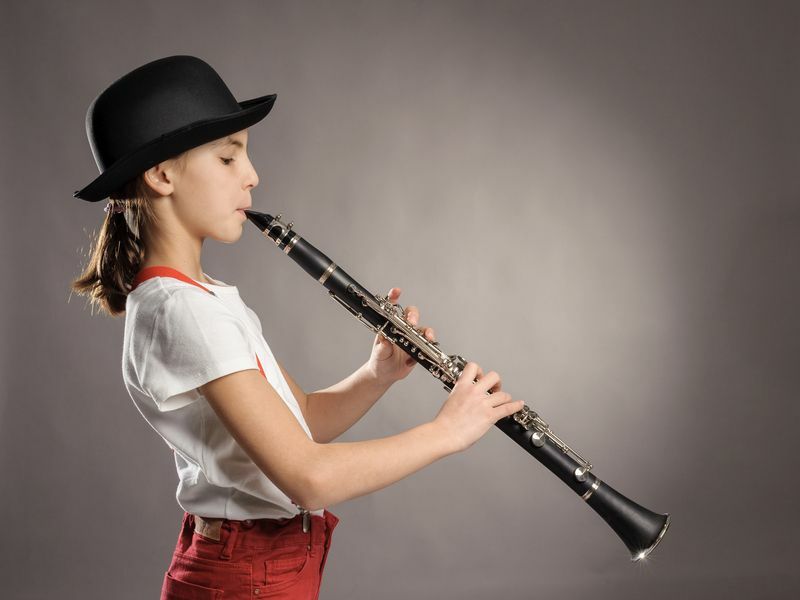 niña pequeña tocando el clarinete en un fondo gris