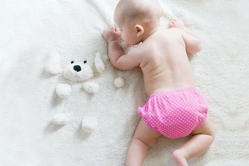 Baby som ligger på forsiden på et fleeceteppe iført en rosa biologisk nedbrytbar bleie.