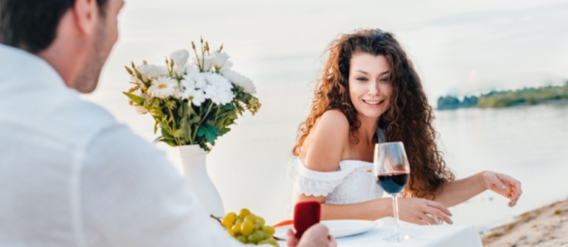 Homem fazendo pedido de casamento com anel para namorada em encontro romântico à beira-mar