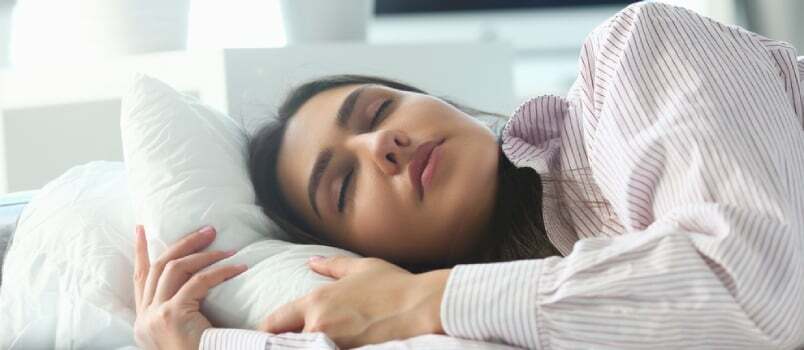 אישה הודית יפה שוכבת בשלווה במיטה ישנה בבוקר מוקדם בזמן שהשעון מעורר הולך לצלצל מתעוררת